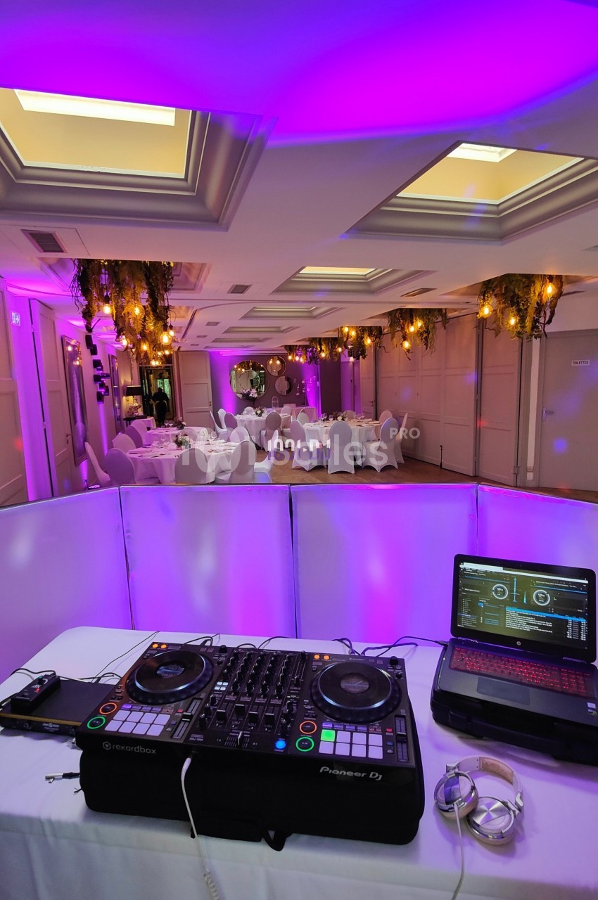 Console de DJ avec ordinateur portable en premier plan, salle de réception décorée et éclairée en violet en arrière-plan.