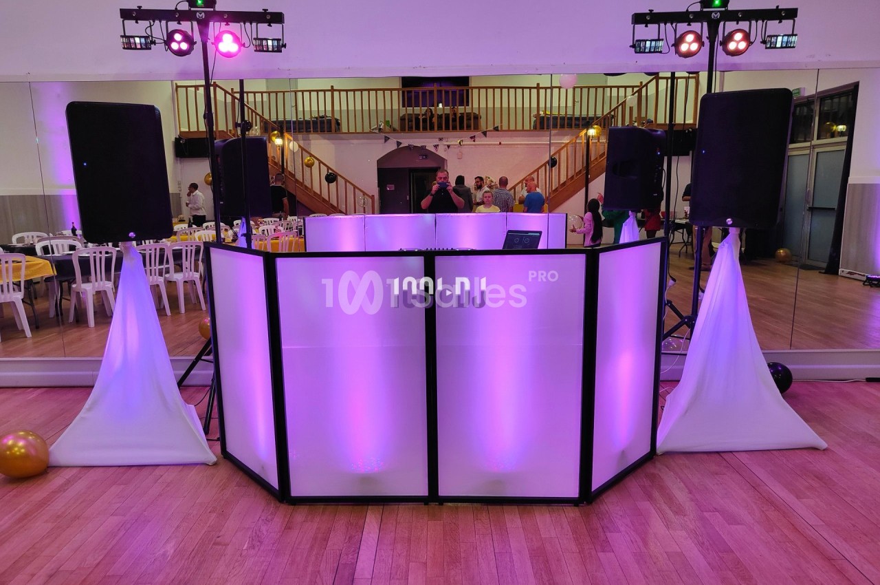 Console de DJ éclairée en violet dans une salle de réception avec des enceintes et des lumières colorées.