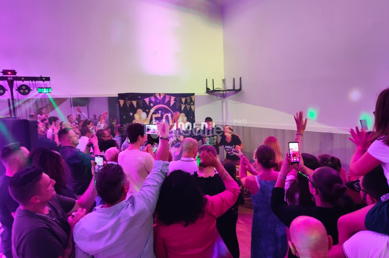 Groupe de personnes debout dans une salle éclairée par des lumières colorées, certaines prenant des photos avec leurs…