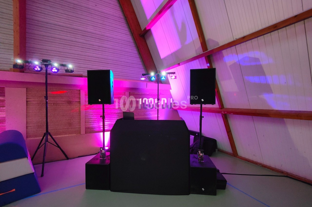 Console de DJ avec enceintes et éclairages colorés dans une salle aux murs en bois et plafond incliné.