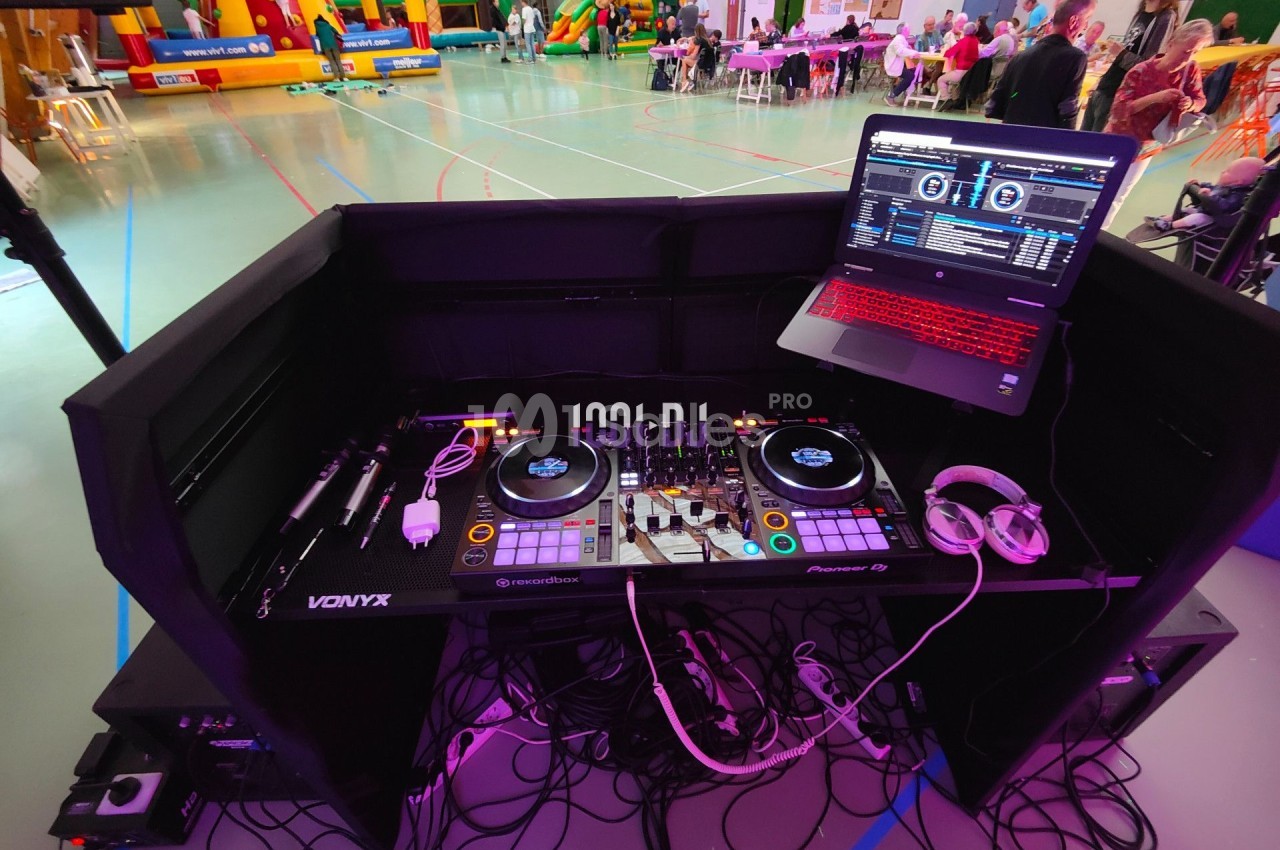 Poste de DJ avec platines, ordinateur portable et casque, installé dans une salle avec structures gonflables en arrière-plan.