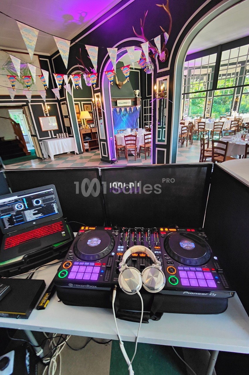 Poste de DJ avec platines, casque et ordinateur dans une salle décorée pour un événement festif.