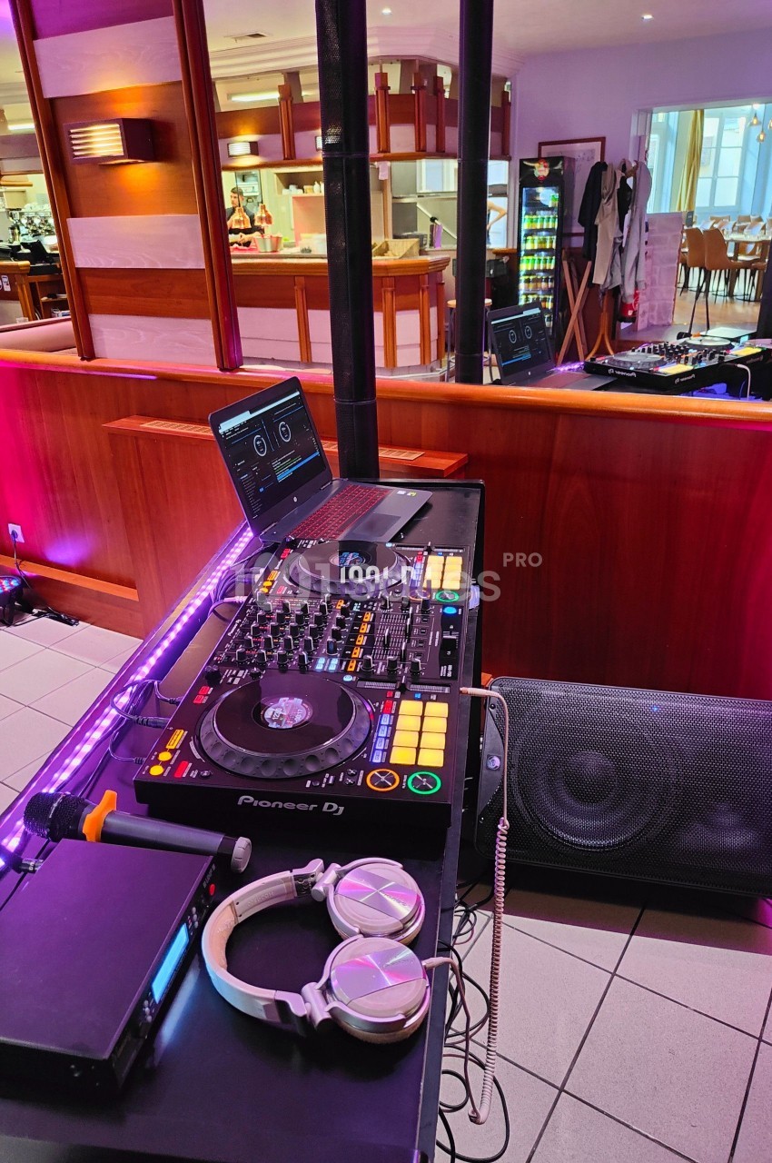 Poste de DJ avec platines, casque audio et ordinateur dans un espace intérieur avec tables et éclairage tamisé.