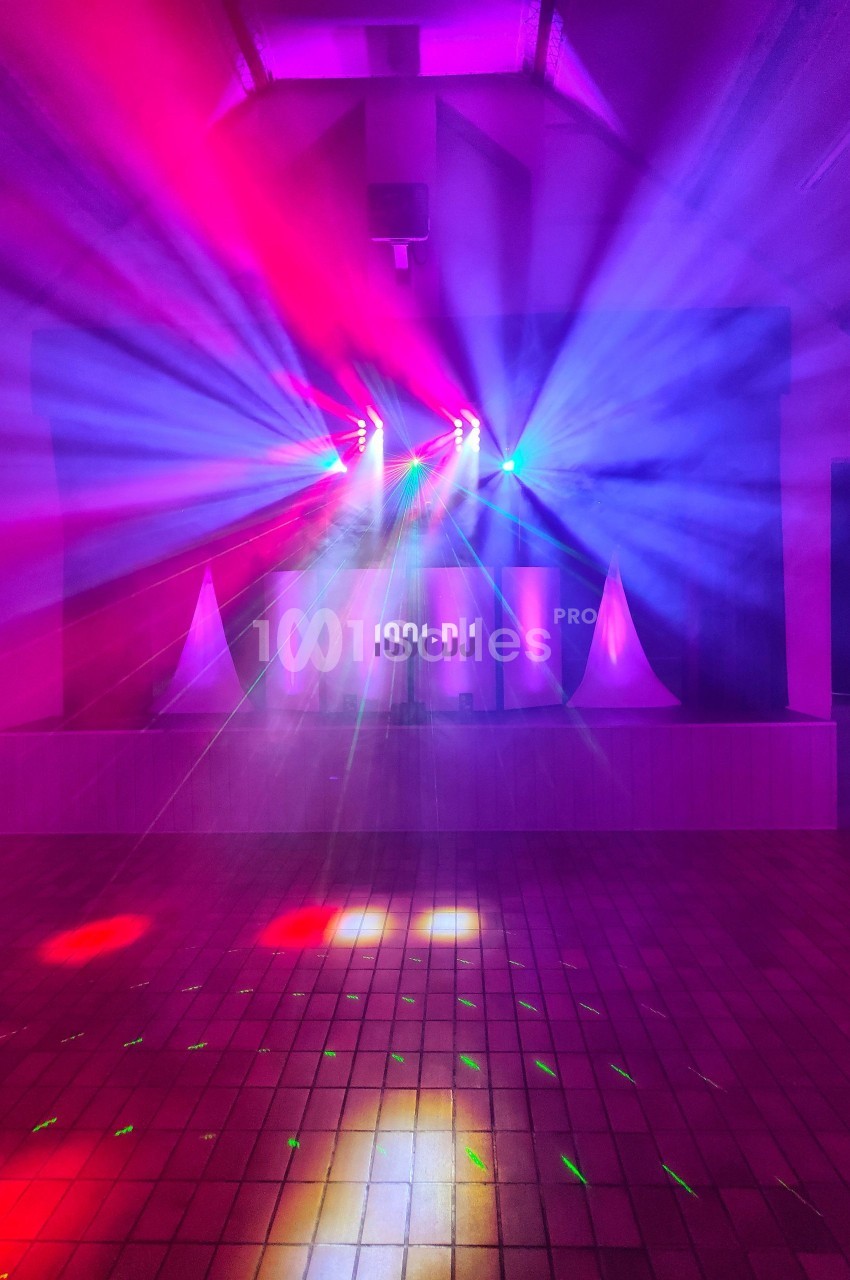 Jeu de lumières colorées projetées dans une salle sombre avec un sol carrelé et un espace de scène.