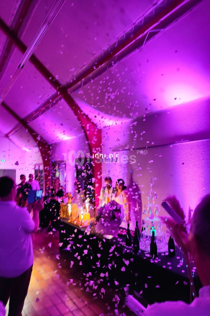 Des confettis tombent dans une salle éclairée de lumières violettes, entourant des personnes célébrant un événement.