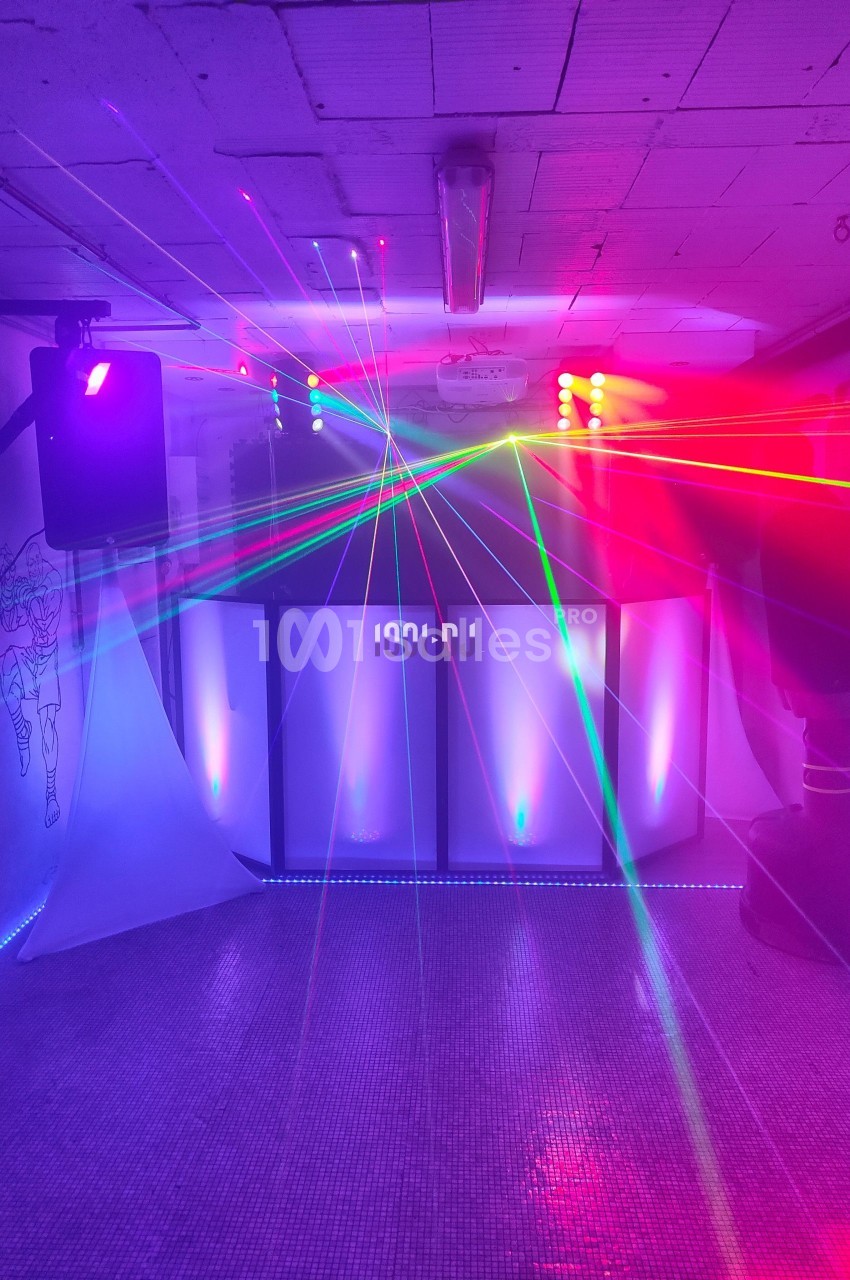 Jeu de lumières colorées et lasers projetés dans une salle sombre avec un espace DJ en arrière-plan.