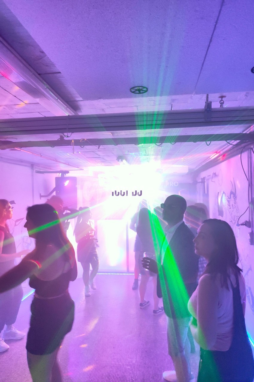 Des personnes dansent dans une pièce éclairée par des lumières colorées et un effet lumineux intense au centre.