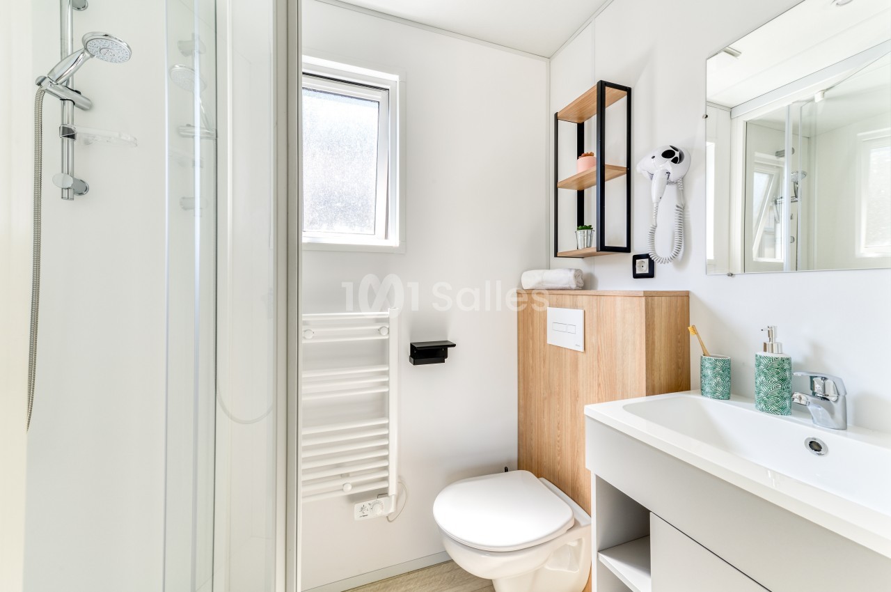 Salle de bain moderne avec douche, lavabo, toilettes suspendues, sèche-serviettes et rangements en bois clair.