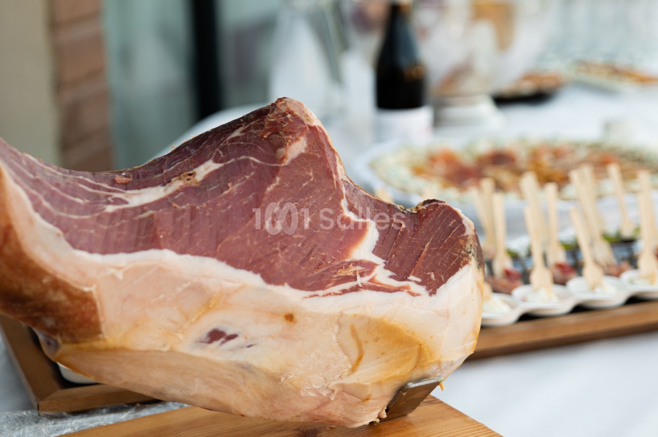 Jambon cru sur un support en bois, avec un buffet flou en arrière-plan.