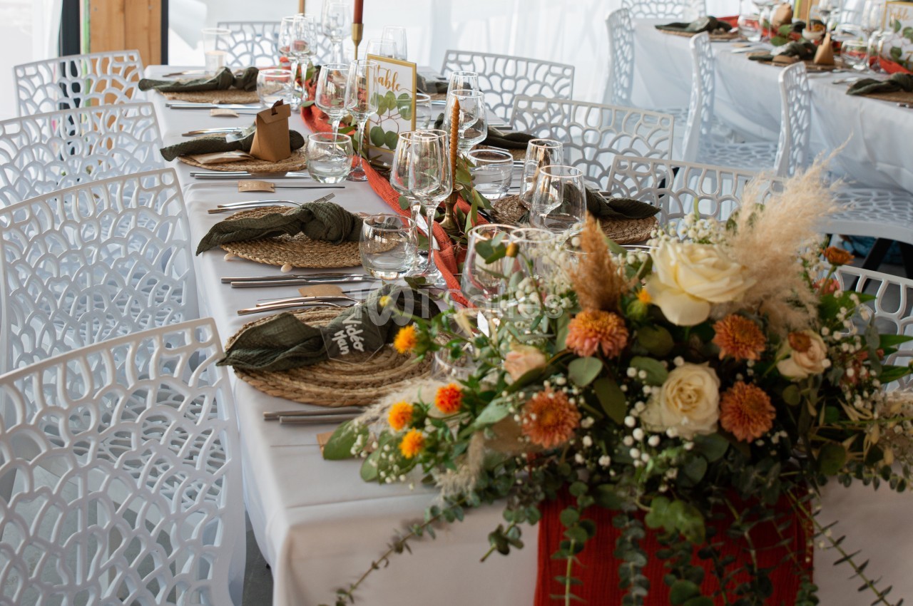 Table dressée avec vaisselle, serviettes pliées, décoration florale colorée et chaises blanches ajourées.