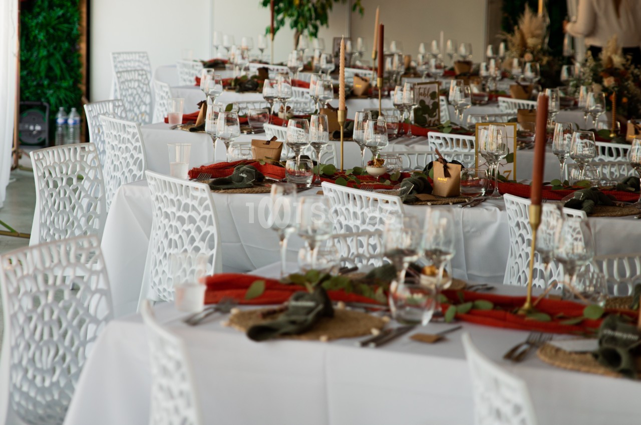 Salle décorée pour un événement avec des tables dressées, nappes blanches, bougies et éléments végétaux.