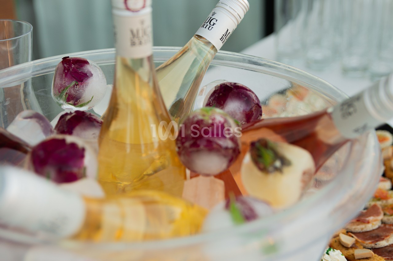 Bouteilles de vin rosé et blanc rafraîchies dans un seau rempli de glaçons et de fleurs congelées.