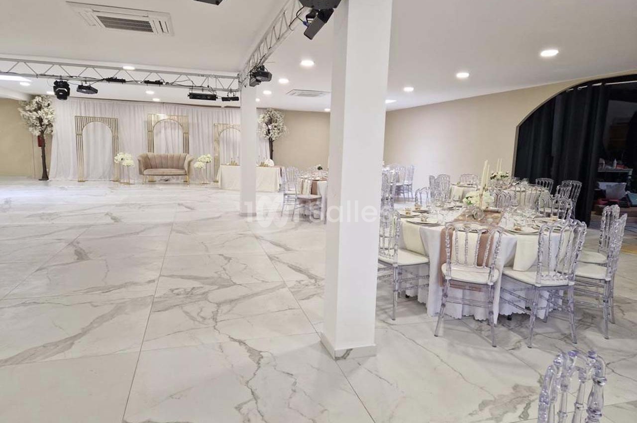 Salle de réception lumineuse avec tables dressées, chaises transparentes et décoration florale élégante.