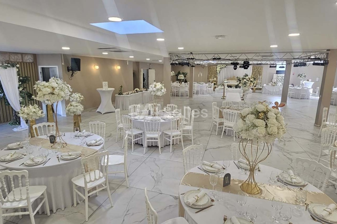Salle de réception élégante avec tables rondes décorées de nappes blanches, fleurs et chaises blanches.