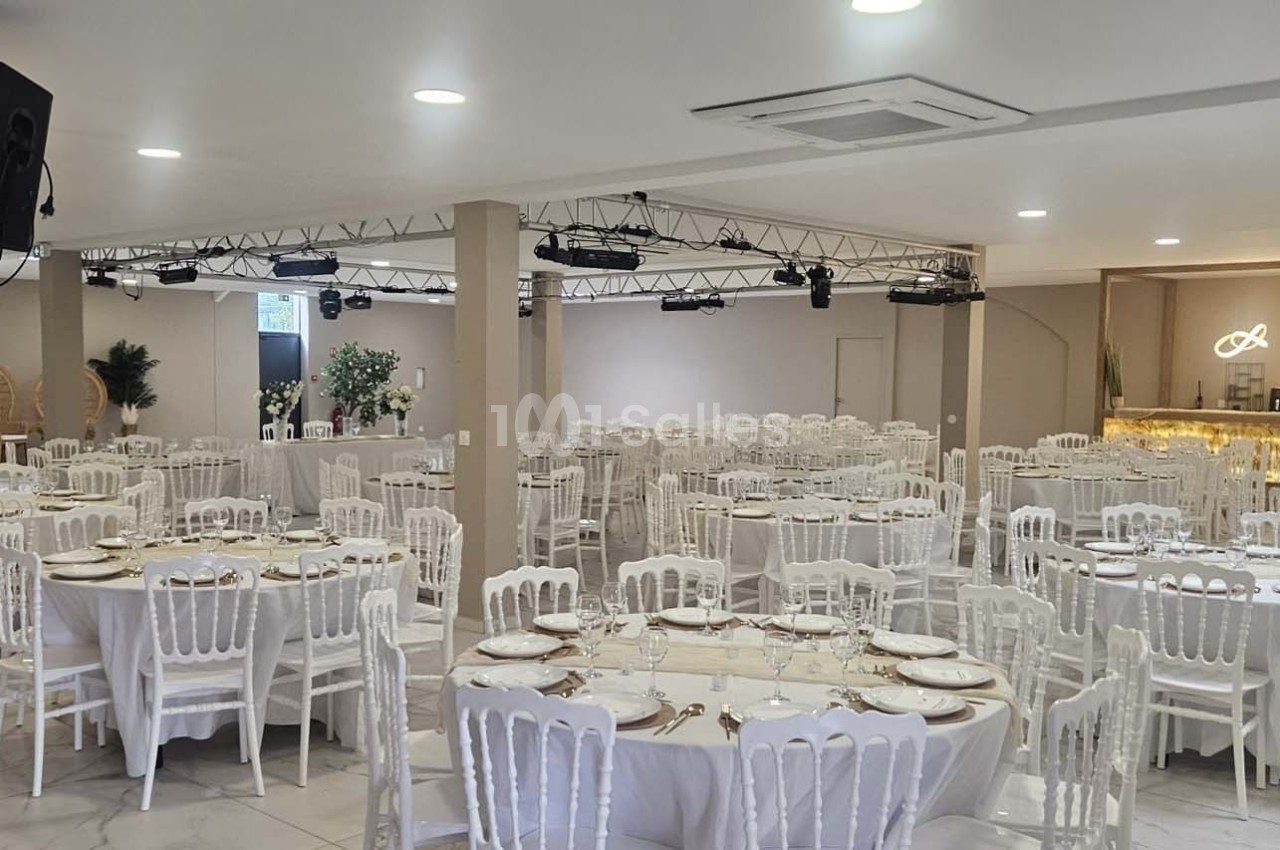 Salle de réception lumineuse avec tables rondes dressées, chaises blanches et décorations élégantes.