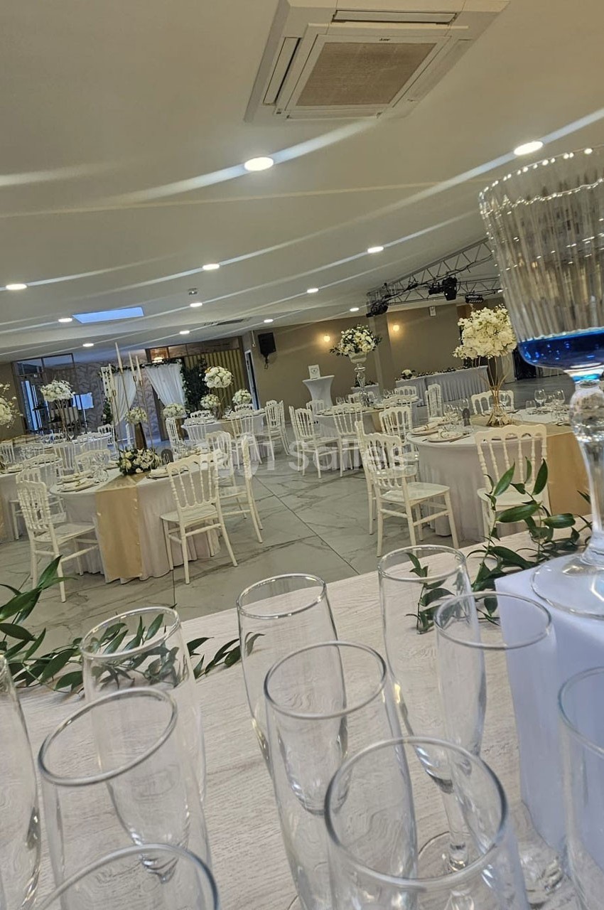 Salle de réception élégamment décorée avec des tables rondes, des chaises blanches et des arrangements floraux.