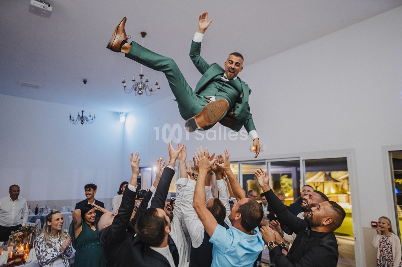 Un homme en costume vert est lancé en l'air par un groupe de personnes lors d'une célébration en intérieur.