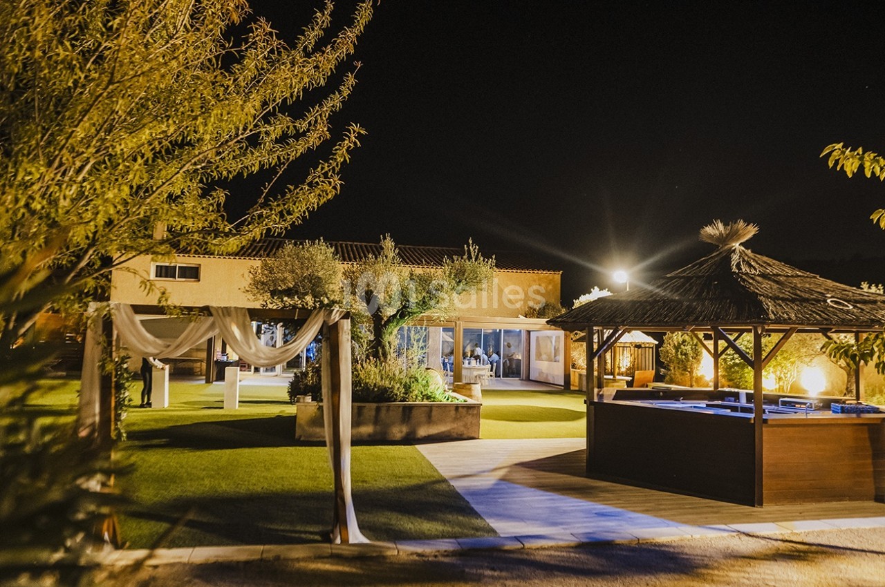 Vue nocturne d'un espace extérieur aménagé avec une pergola, un jacuzzi et un jardin éclairé.