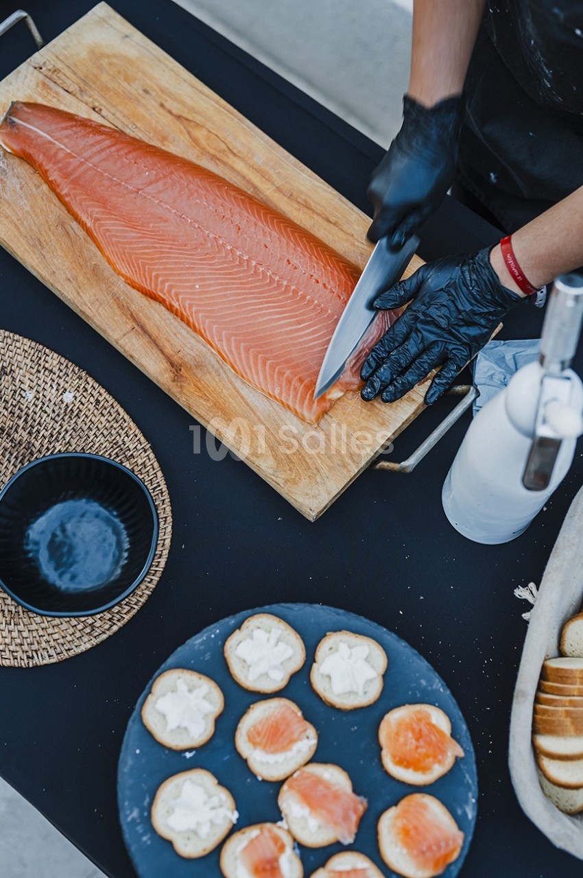 Une personne tranche un filet de saumon sur une planche en bois, avec des toasts préparés en premier plan.