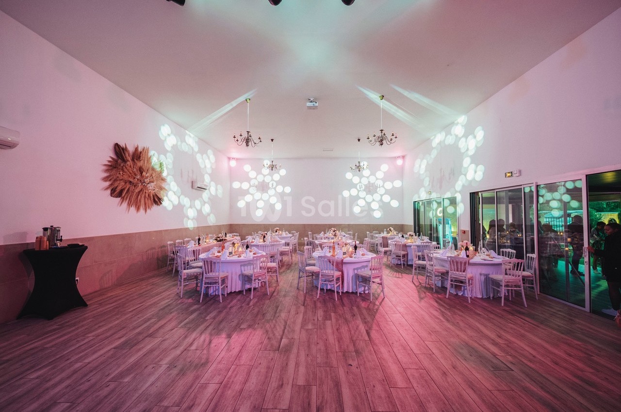 Salle de réception décorée avec des tables rondes dressées, éclairage tamisé et motifs lumineux sur les murs.