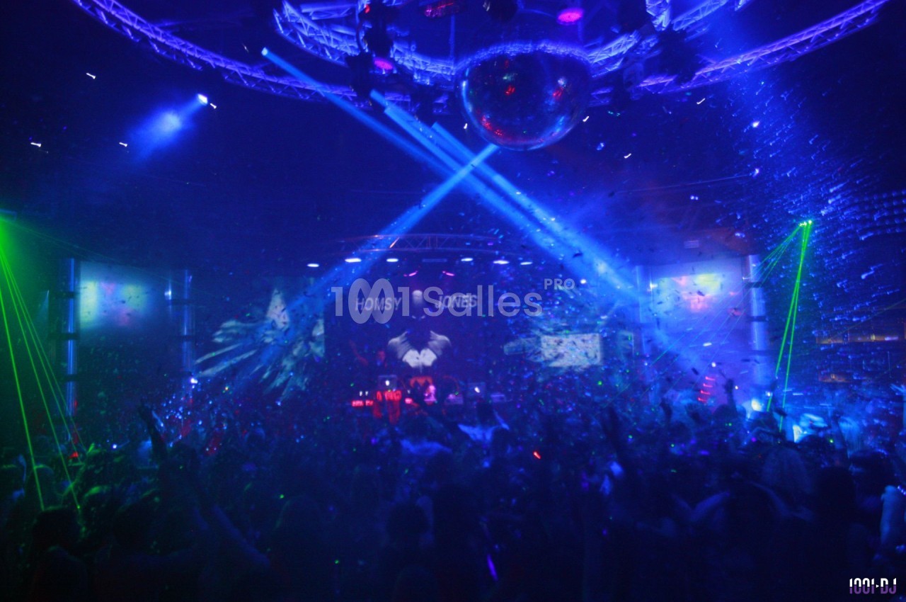 Foule dans une discothèque sombre avec des jeux de lumières colorées, une boule disco et une scène illuminée.