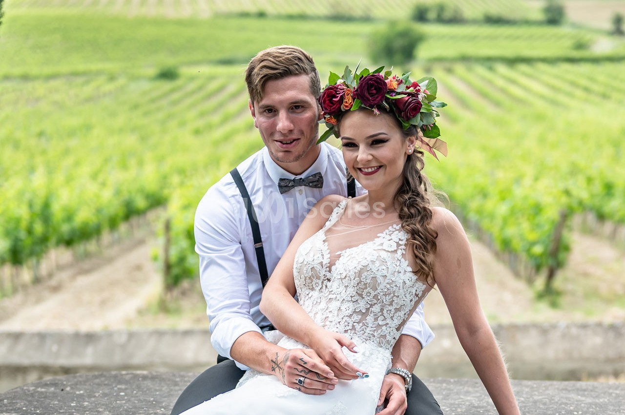 Un couple de mariés sourit devant un paysage de vignobles verdoyants.
