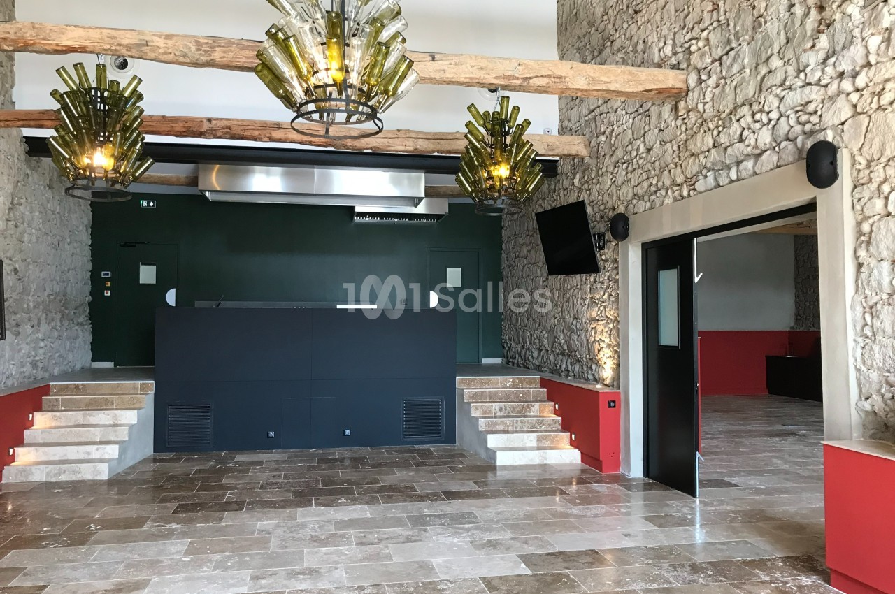 Salle intérieure avec murs en pierre, lustres en bouteilles recyclées, sol en pierre et comptoir noir central.
