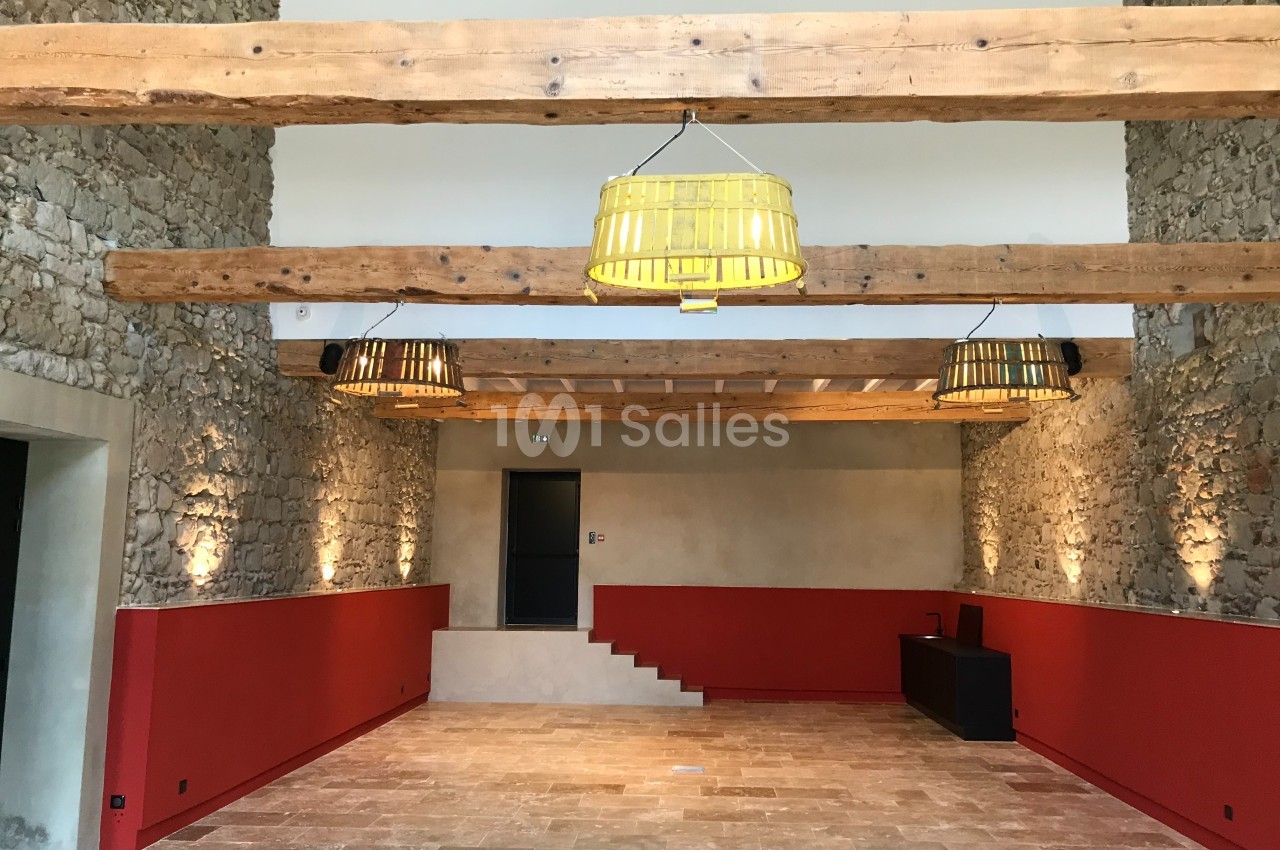Salle intérieure avec murs en pierre, poutres apparentes, suspensions jaunes et rouges, et sol en pierre beige.