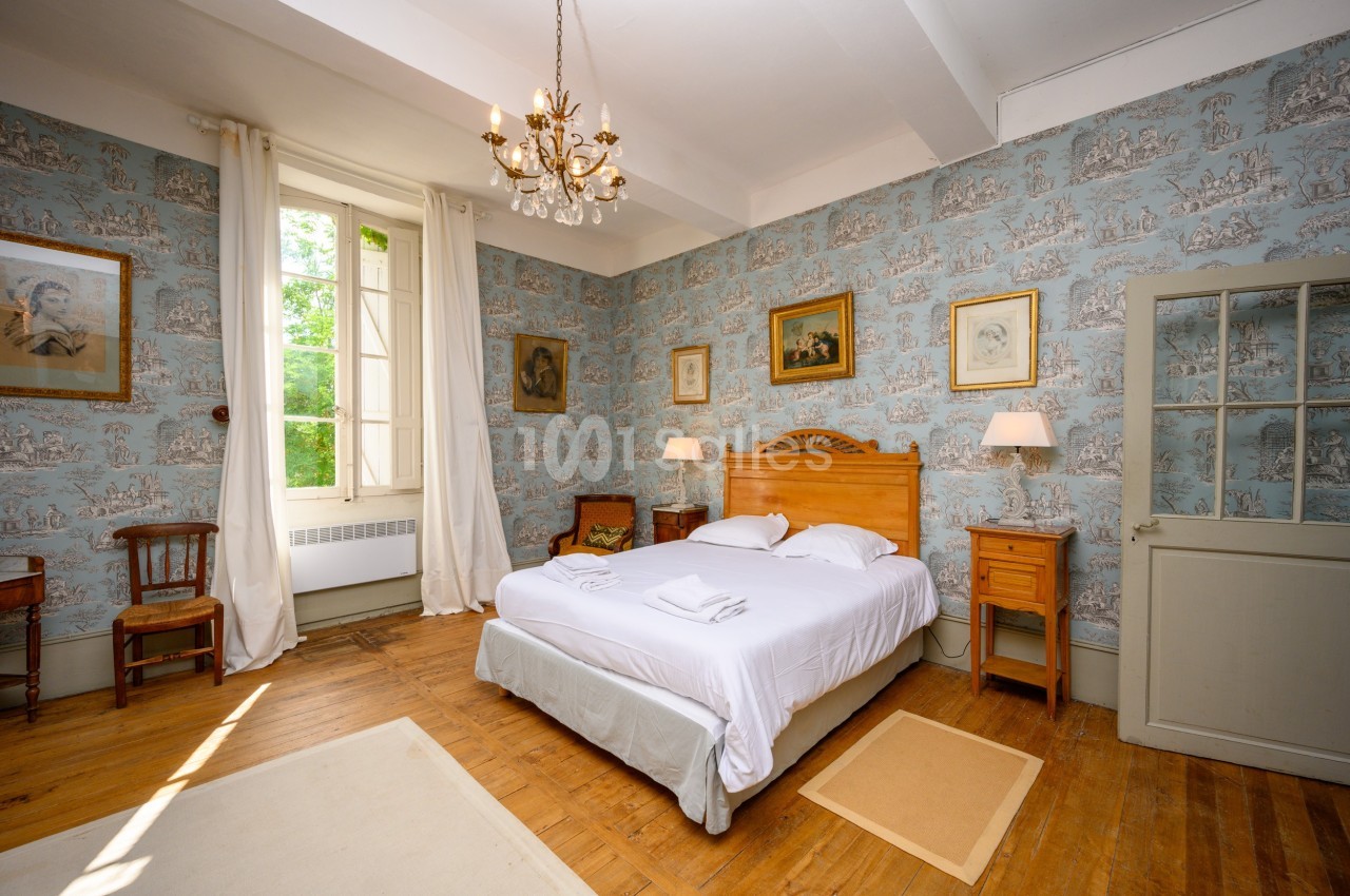 Chambre lumineuse avec lit double, parquet, murs décorés de papier peint bleu et mobilier en bois classique.
