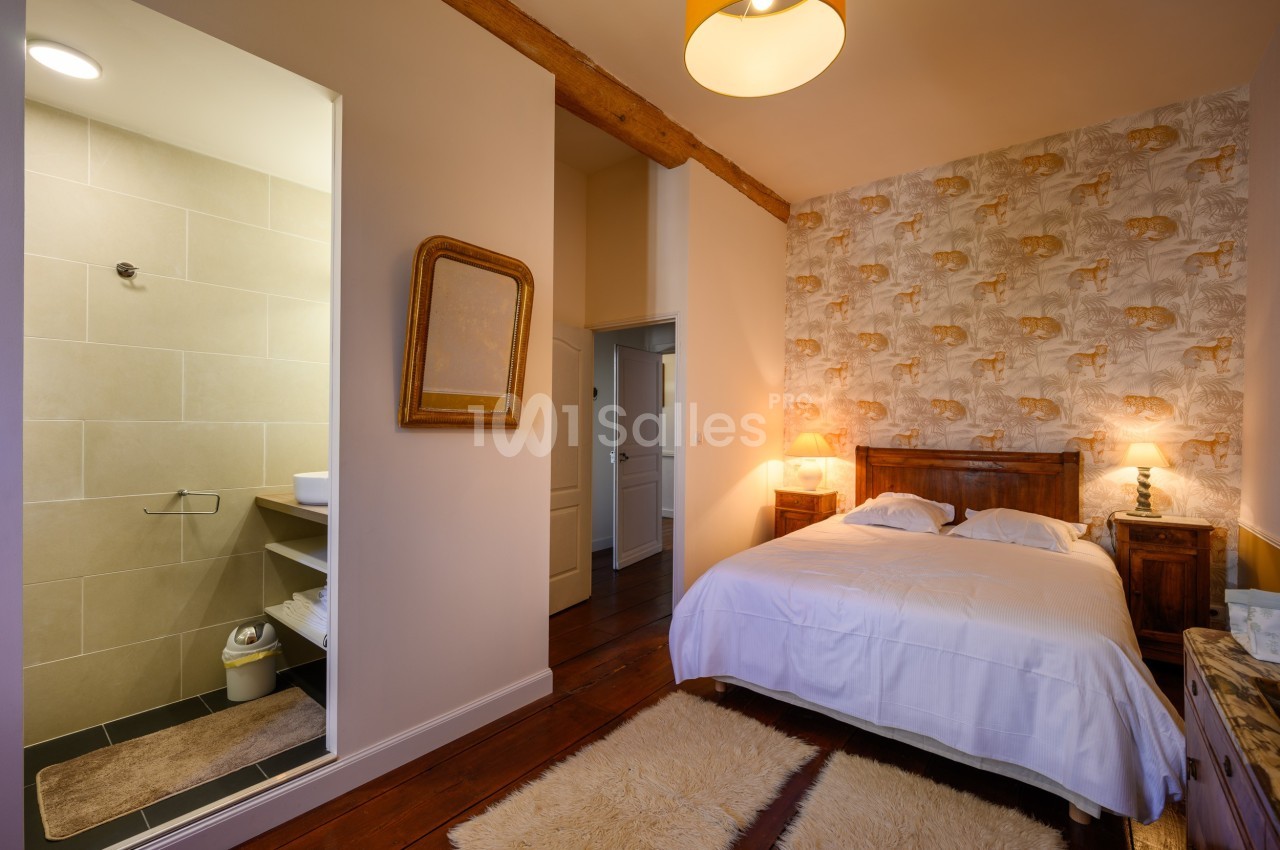 Chambre avec lit double, murs décorés, tapis au sol, et salle de bain attenante avec douche visible.