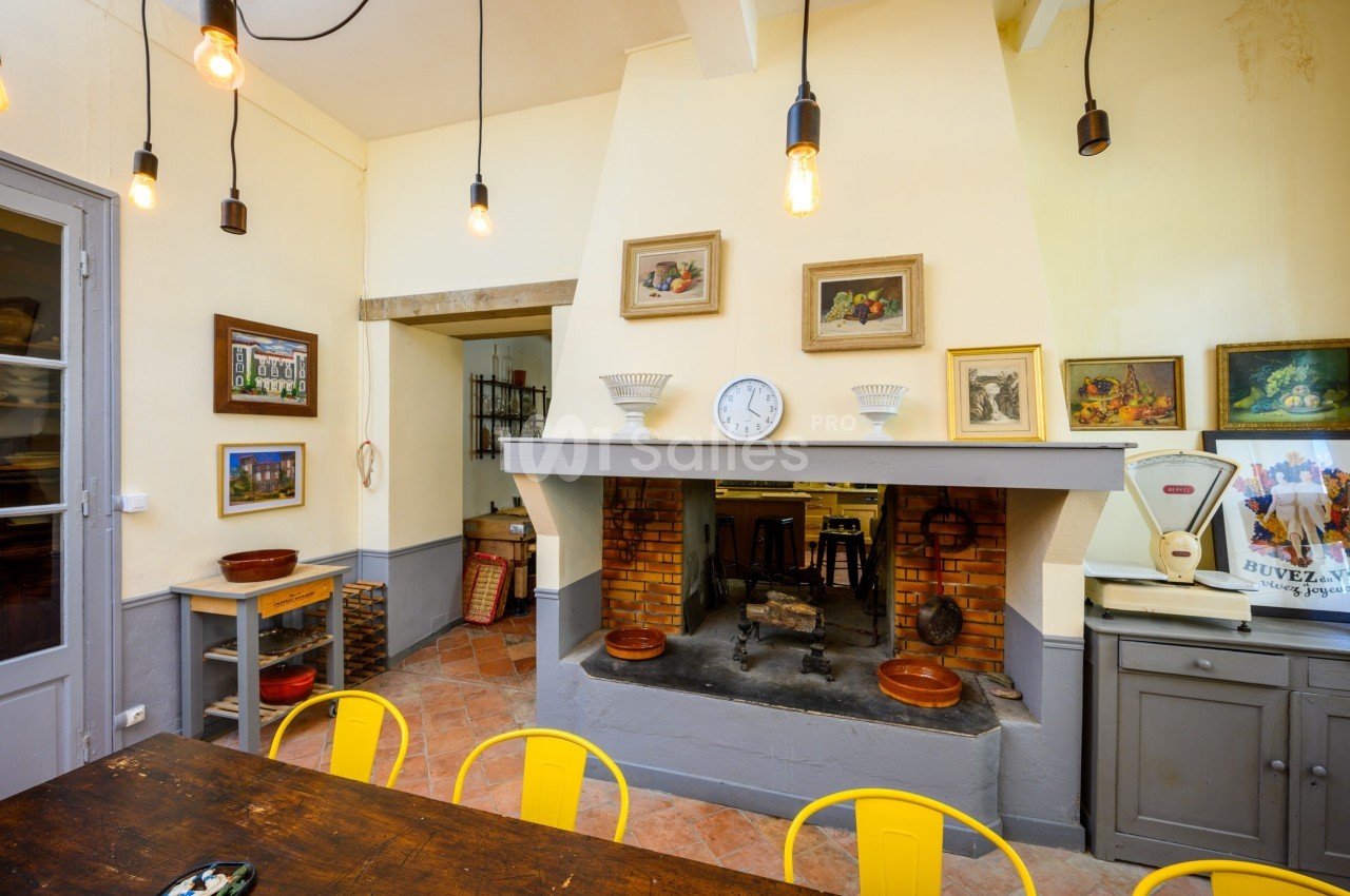 Cuisine rustique avec cheminée en briques, table en bois, chaises jaunes et décorations murales.