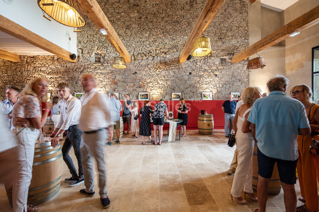 Personnes rassemblées dans une salle lumineuse avec murs en pierre, poutres apparentes et expositions murales.