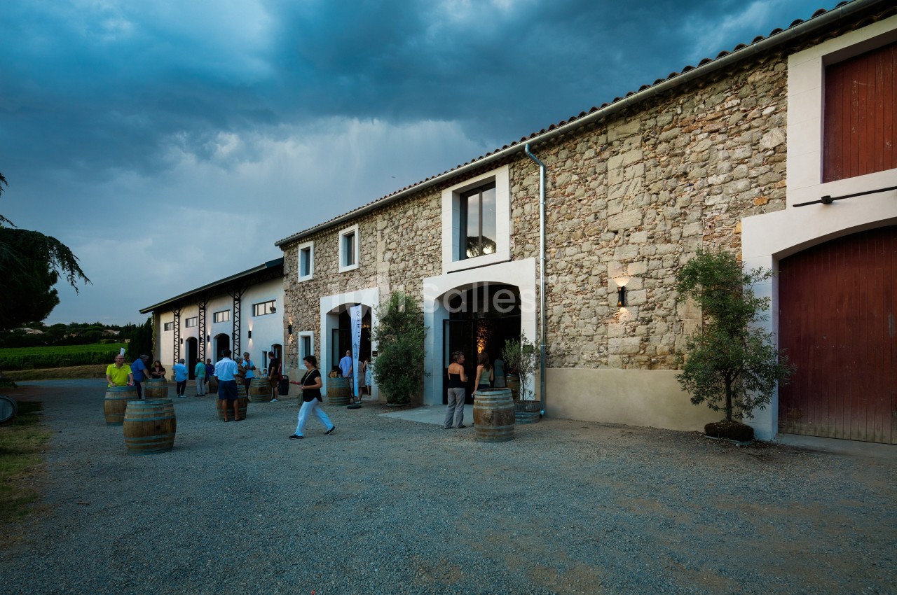 Façade en pierre d'un domaine viticole avec des visiteurs entrant et sortant sous un ciel nuageux.