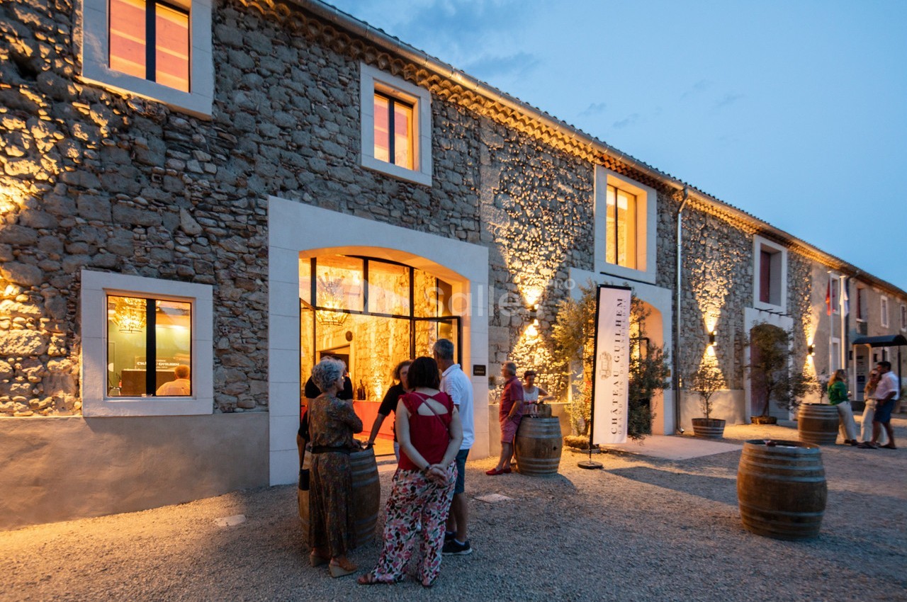 Façade en pierre éclairée d'un bâtiment avec des visiteurs rassemblés devant l'entrée au crépuscule.