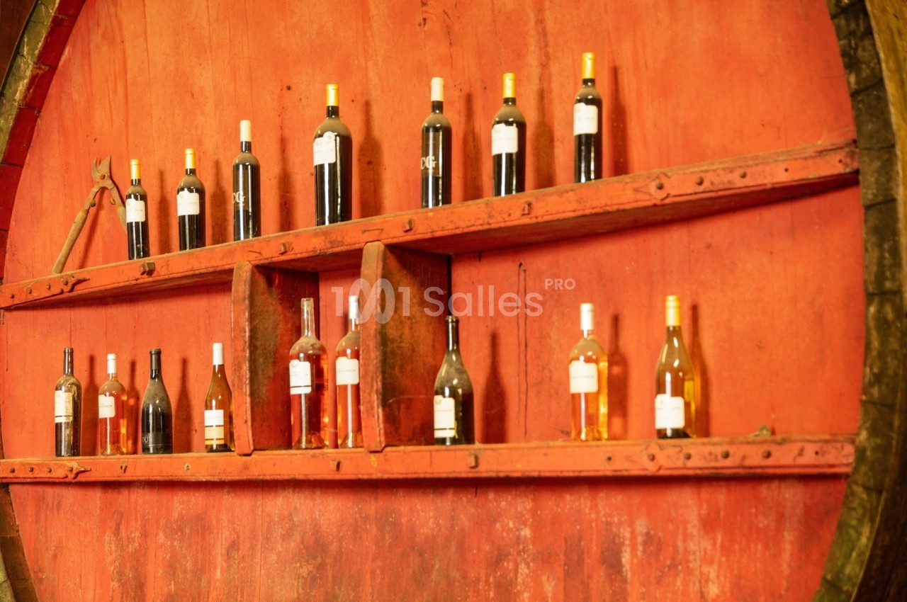 Bouteilles de vin rouge, blanc et rosé alignées sur des étagères fixées à un grand tonneau en bois rouge.