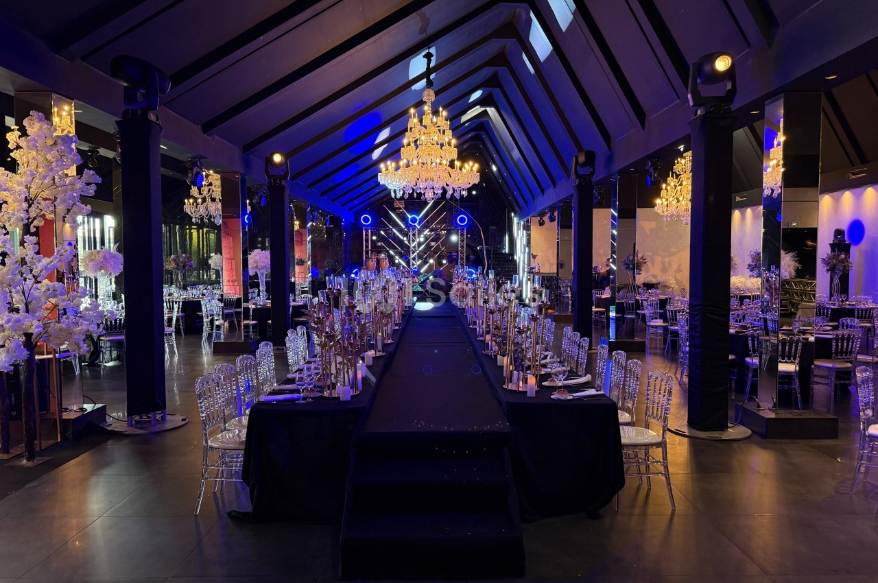 Salle de réception élégante avec tables dressées, chandeliers lumineux et éclairage bleu tamisé.