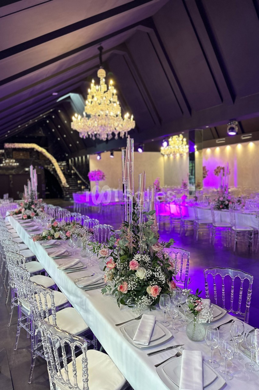 Salle de réception élégante avec tables décorées de fleurs roses et chandeliers lumineux suspendus.