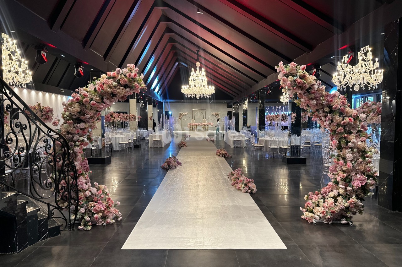 Salle de réception élégante avec allée centrale bordée d'arcs fleuris et lustres suspendus.