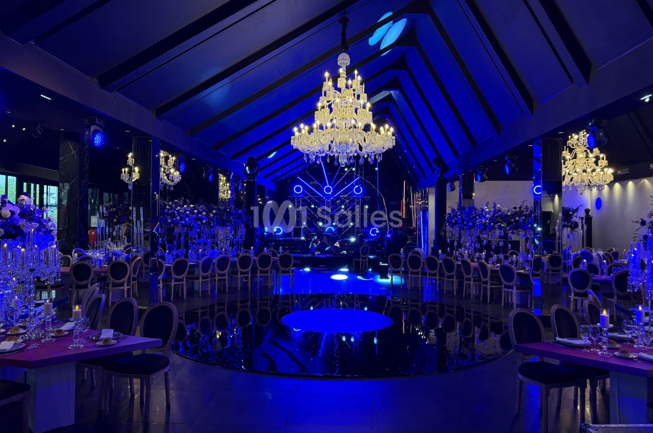 Salle de réception élégante avec éclairage bleu, lustres imposants et tables dressées pour un événement.