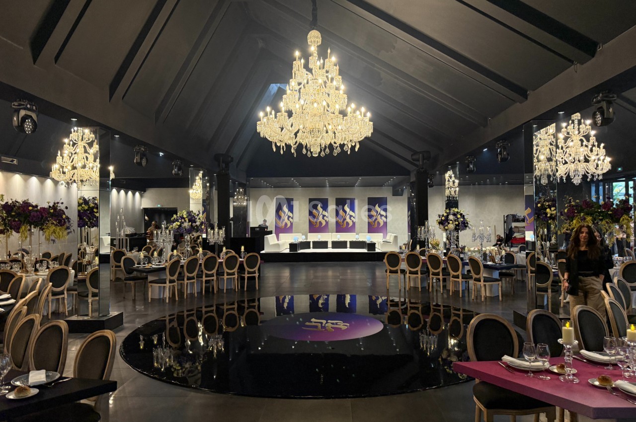 Salle de réception élégante avec lustres en cristal, tables dressées et décorations florales colorées.
