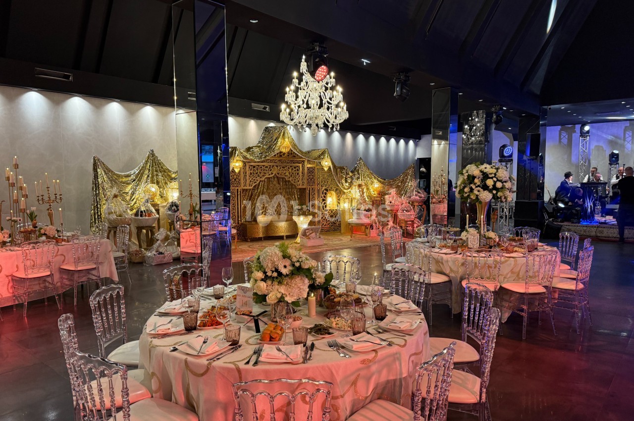 Salle de réception décorée avec des tables élégantes, des chaises transparentes et un espace orné de rideaux dorés.