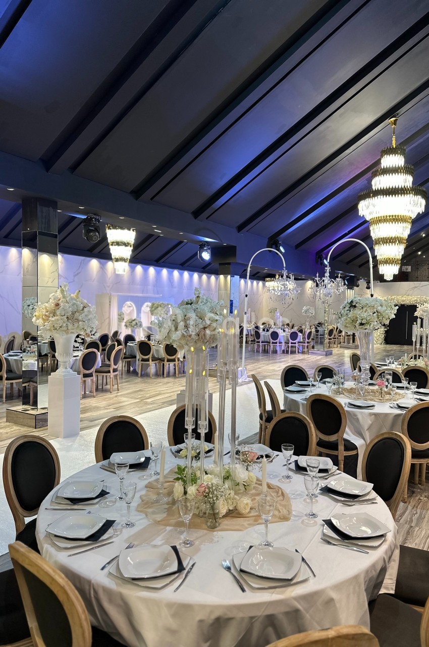 Salle de réception élégante avec tables dressées, décor floral blanc et lustres imposants sous un plafond voûté.
