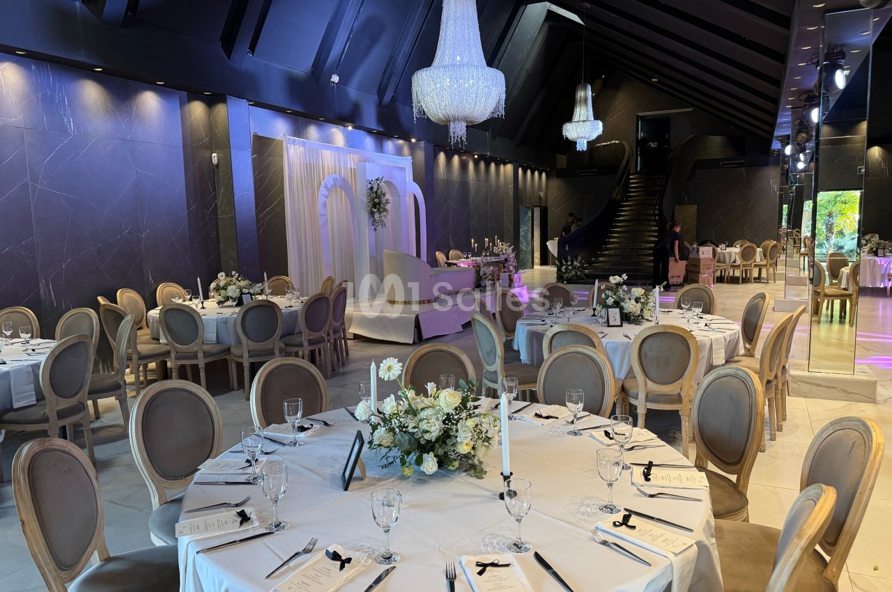 Salle de réception élégante avec tables rondes dressées, chandeliers suspendus et décor floral raffiné.