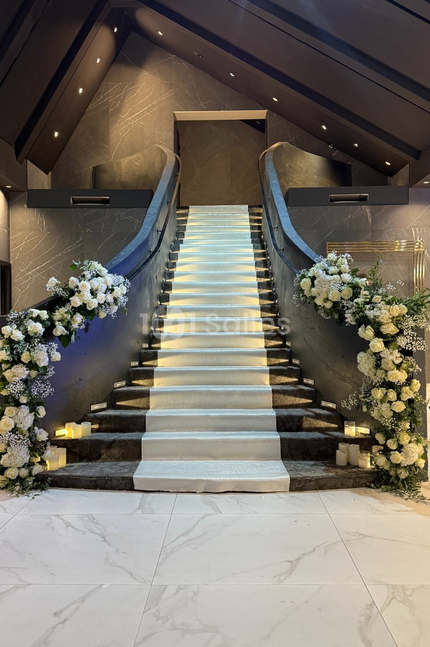 Escalier central élégant avec rampe noire, décoré de fleurs blanches et éclairé par des lumières tamisées.