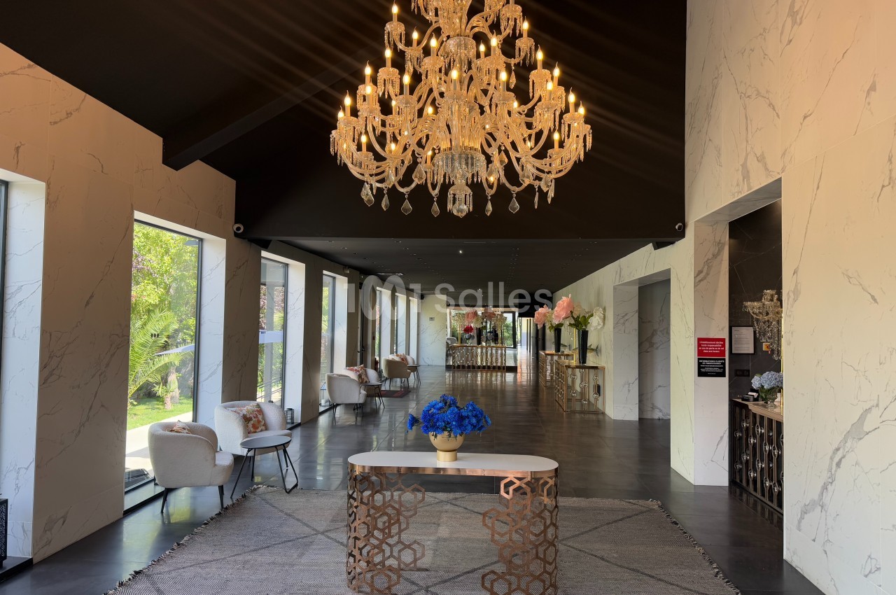 Hall élégant avec un lustre en cristal, un bureau décoré de fleurs bleues et des fauteuils près de grandes fenêtres.