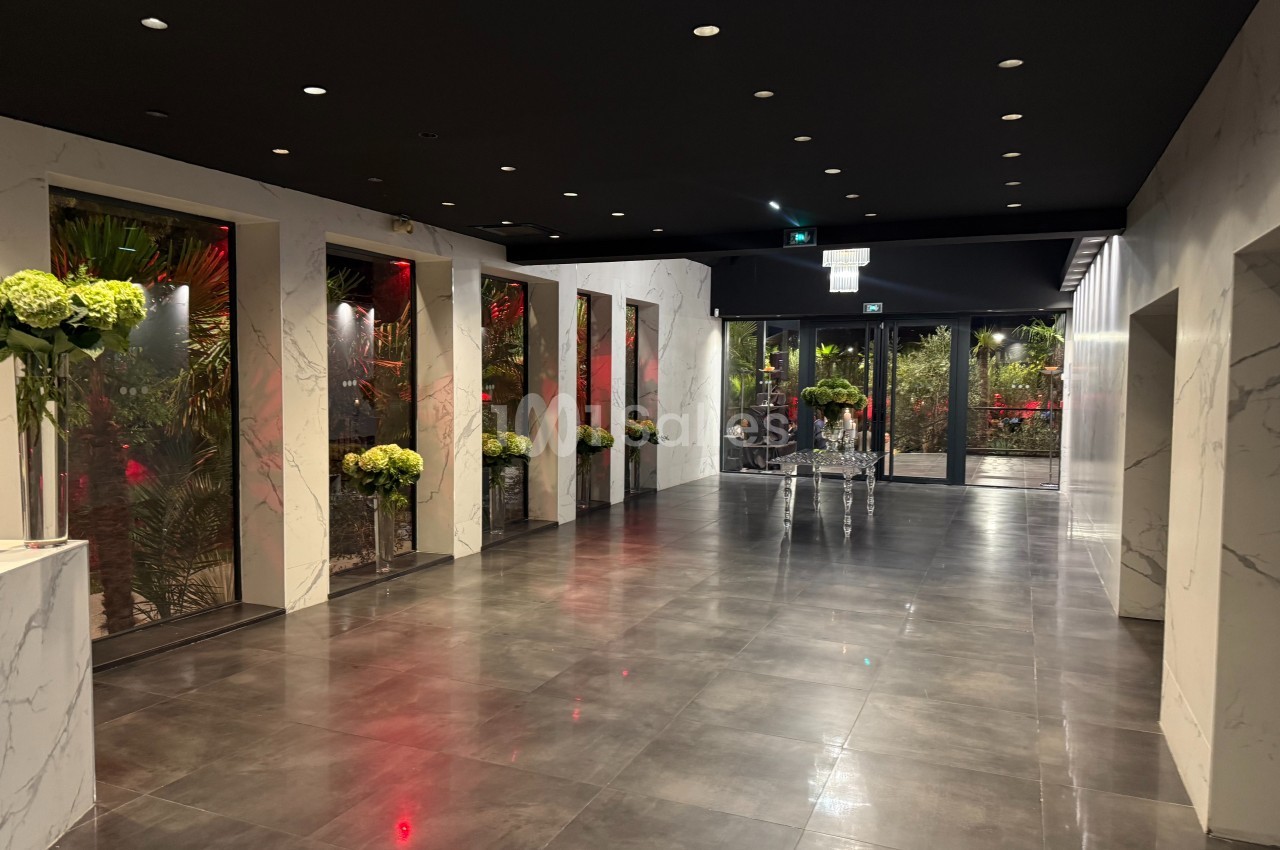 Couloir moderne avec sol en carrelage sombre, murs effet marbre, éclairage tamisé et décorations florales.