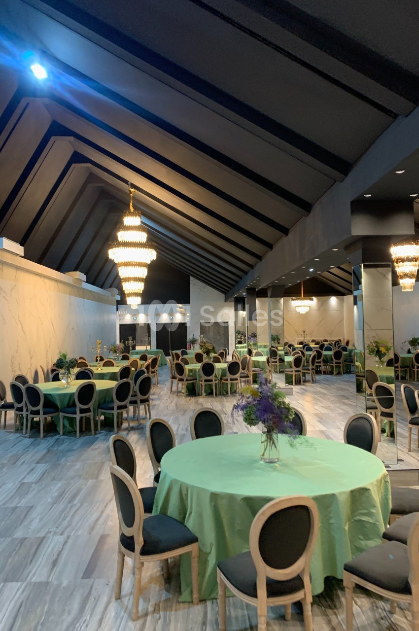 Salle de réception élégante avec tables rondes couvertes de nappes vertes, chaises noires et lustres imposants.
