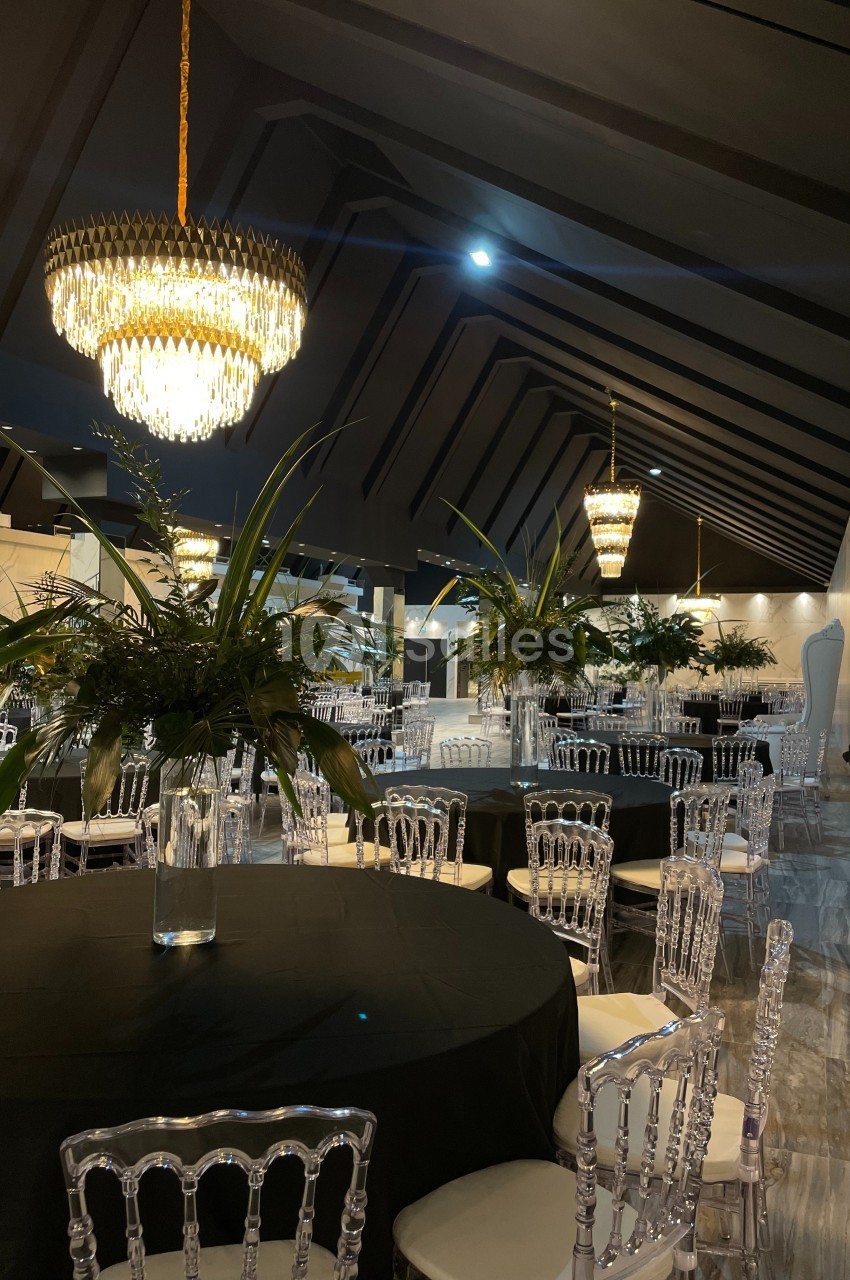 Salle de réception élégante avec tables rondes noires, chaises transparentes, lustres en cristal et décorations végétales.