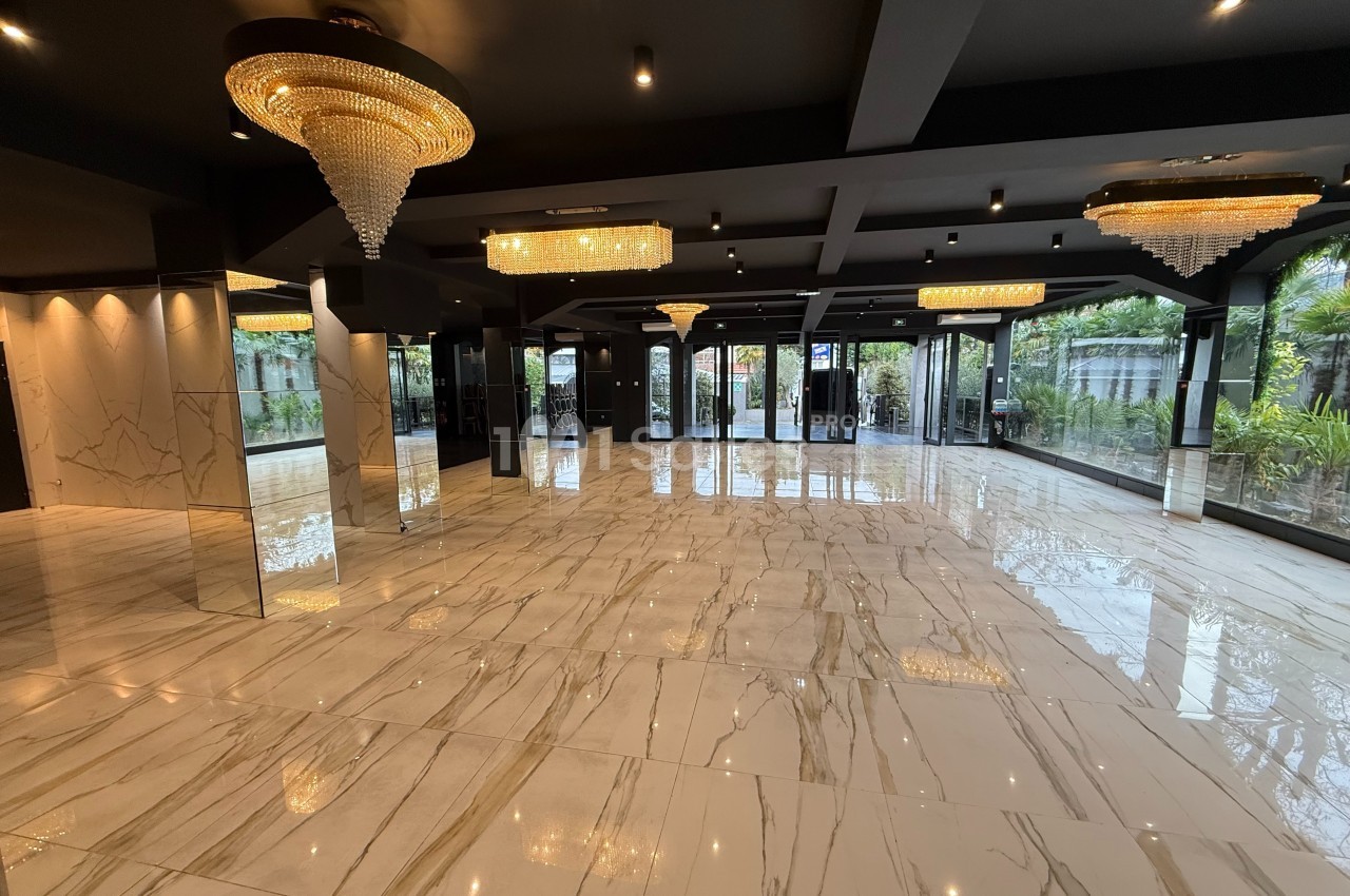 Salle spacieuse avec sol en marbre, lustres en cristal et grandes baies vitrées donnant sur un jardin.