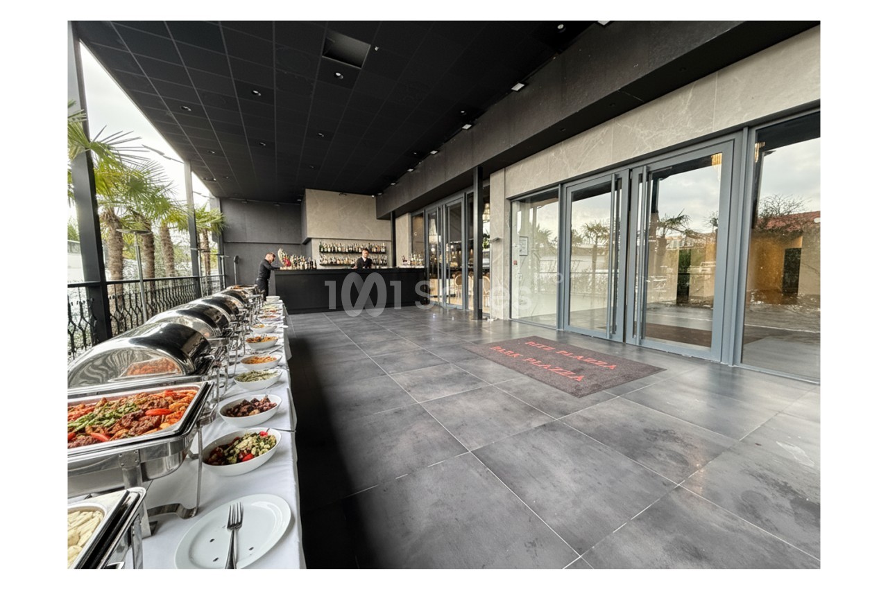 Buffet varié disposé sur une terrasse moderne avec vue sur des palmiers et un bar en arrière-plan.